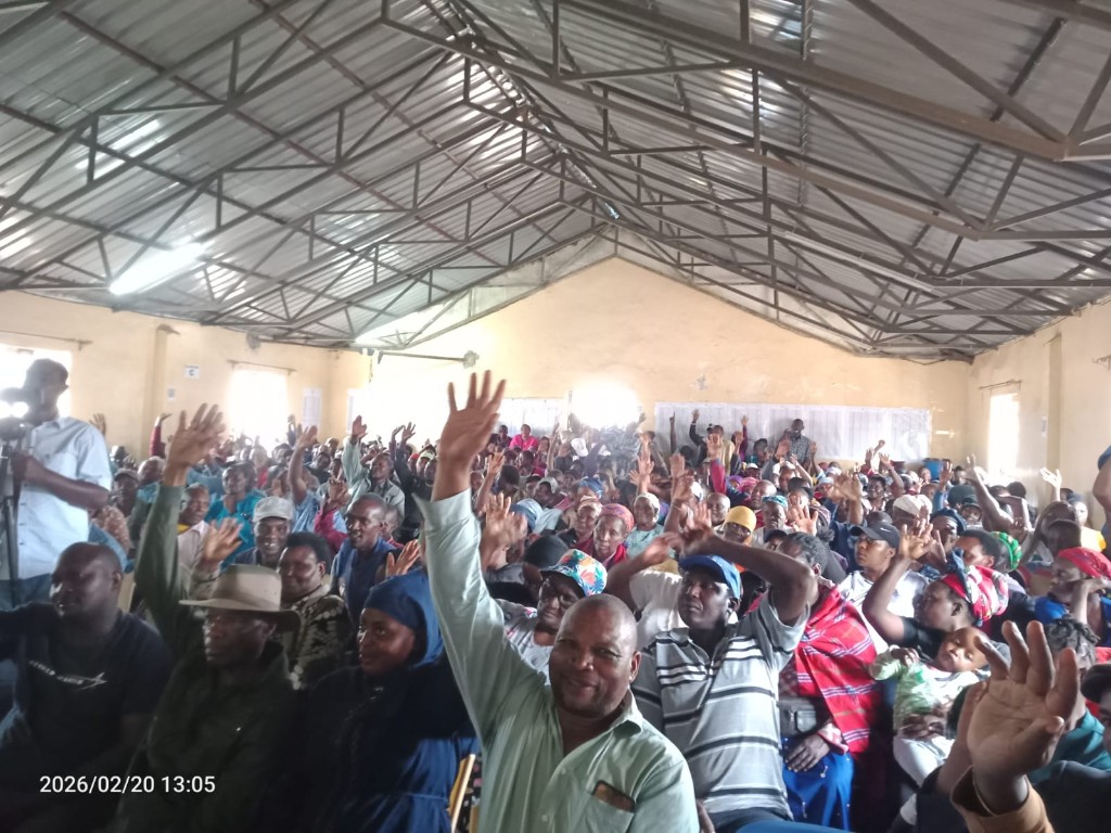Large community gathering in a hall with many participants raising hands in agreement during a forum